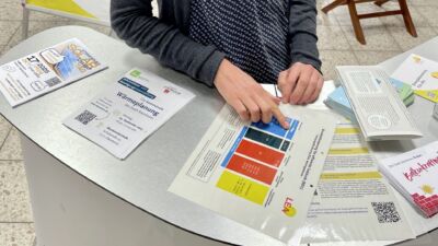 Energieberaterin der LEA steht an einem Stand mit vielen Info-Materialien in einer Einkaufspassage